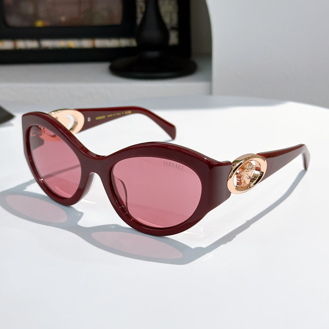 Burgundy cat-eye sunglasses with gold medallion logo detail and pink tinted lenses