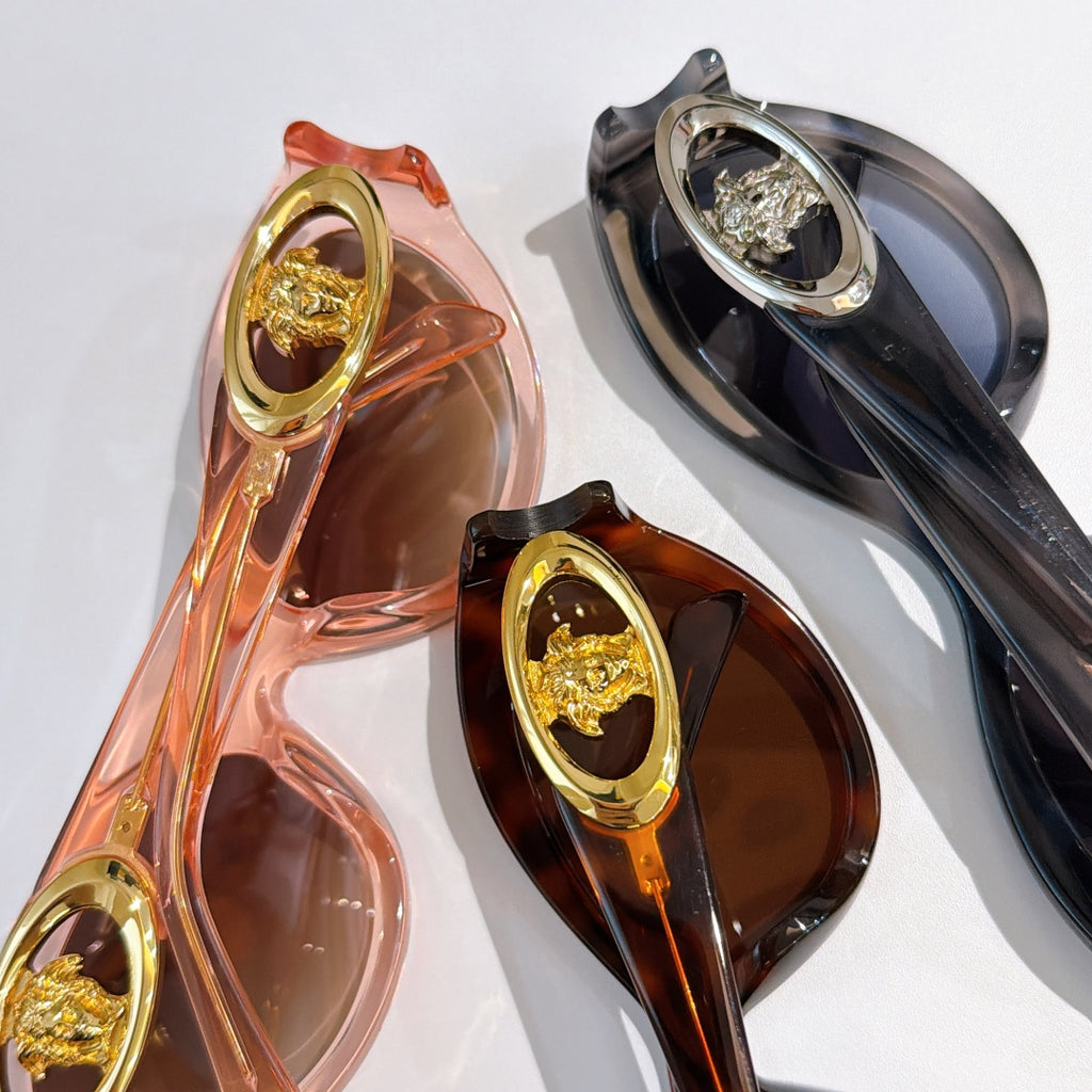 Close-up of two sunglasses frames with gold medallion details in pink/orange and dark