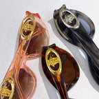 Close-up of two sunglasses frames with gold medallion details in pink/orange and dark
