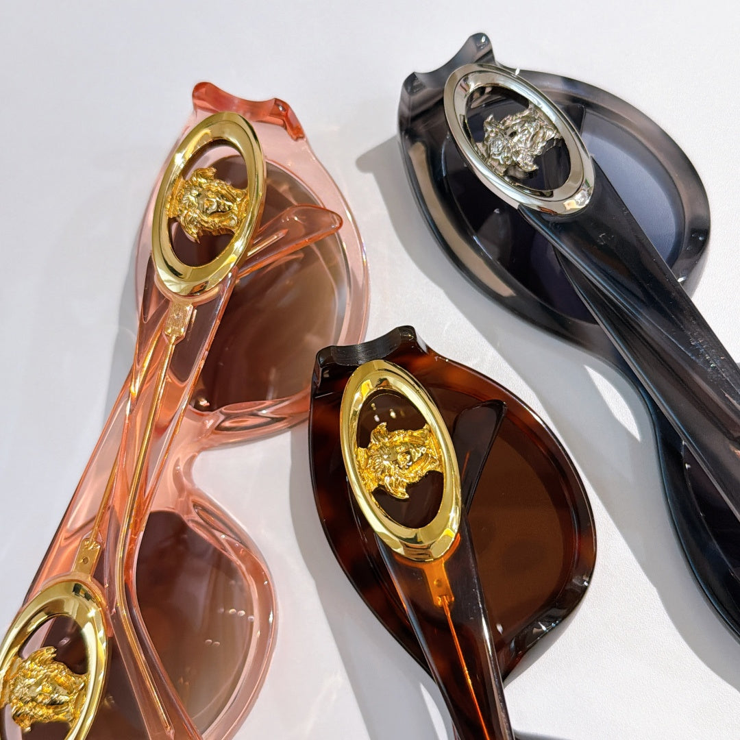 Close-up of two sunglasses frames with gold medallion details in pink/orange and dark