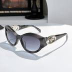 Dark gray cat-eye sunglasses with gold medallion logo detail and tinted lenses