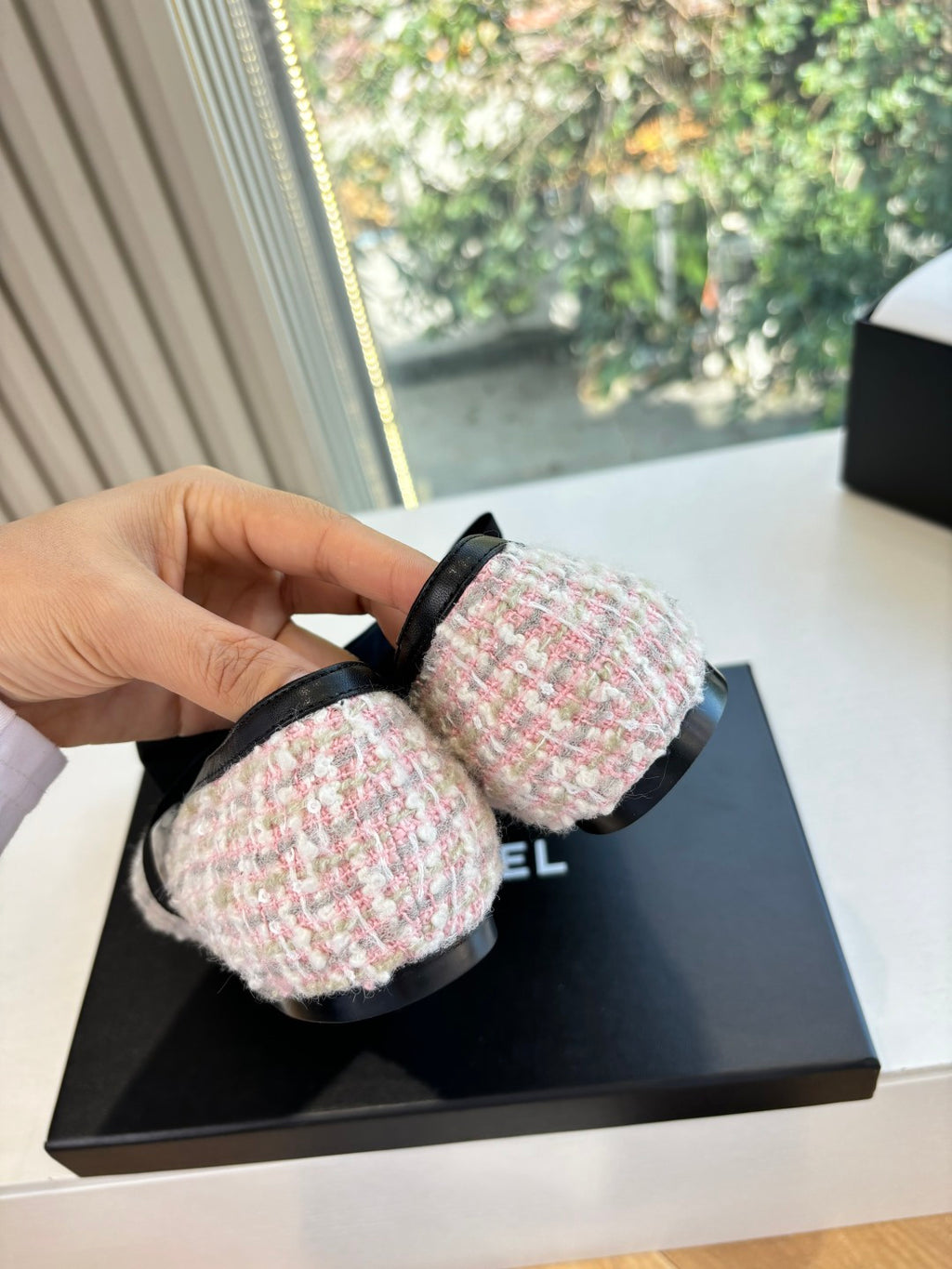 Hand holding black and tweed ballet flat with ribbon bow near front opening