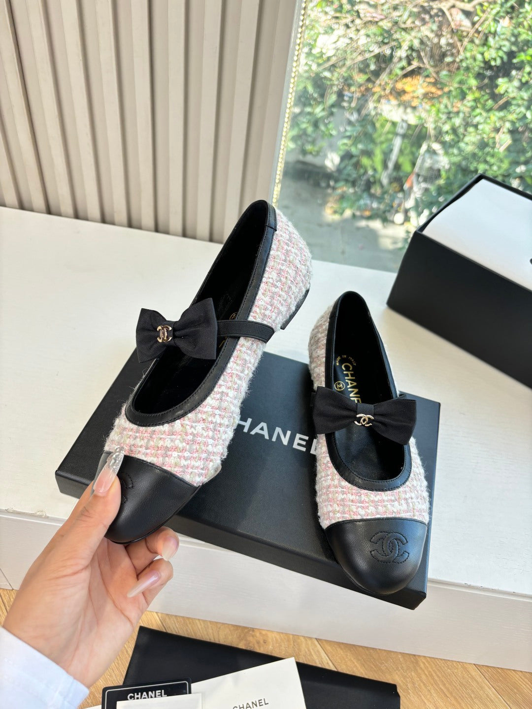 Black and tweed ballet flats with front bow detail, shown beside branded boxes