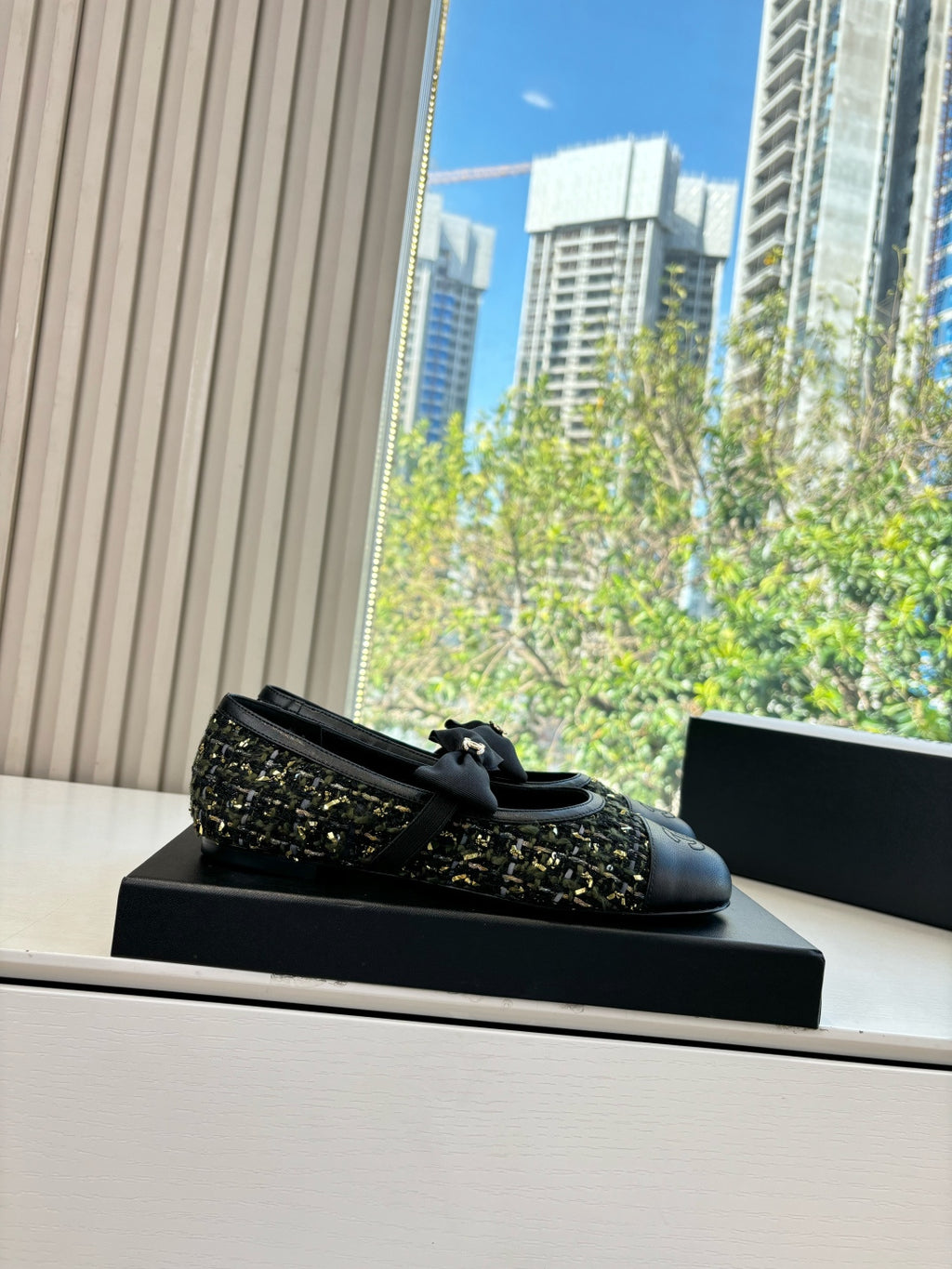 Black Chanel loafers with bow and multicolor tweed upper, sitting on box