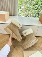 Tan suede ankle boots with white shearling cuffs and side emblem, held in hand