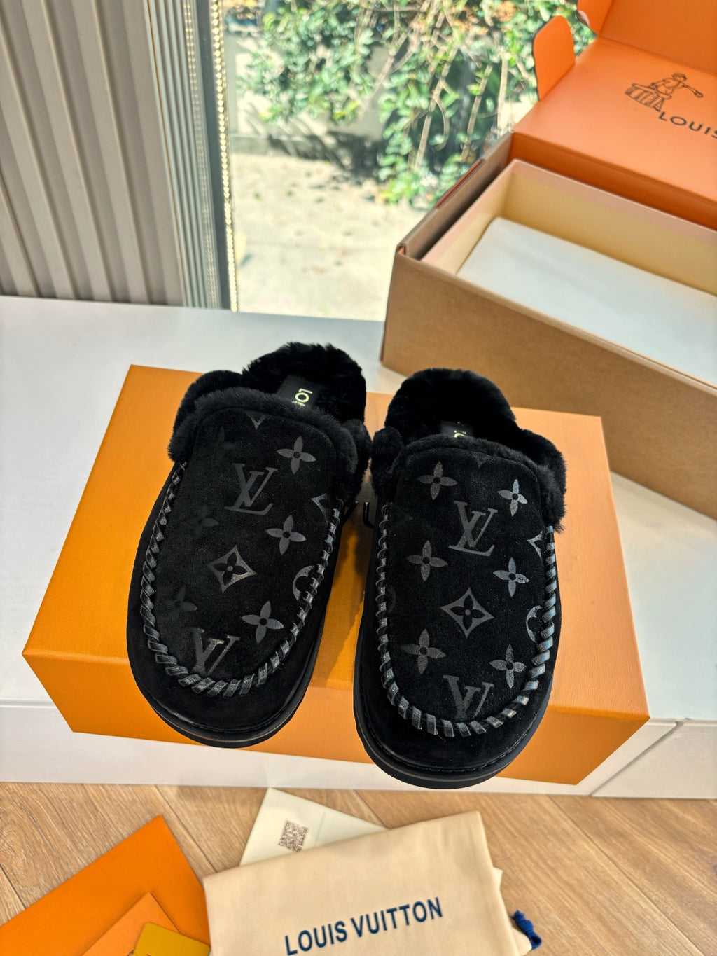 Black Louis Vuitton monogram slippers with plush lining, front view on orange box
