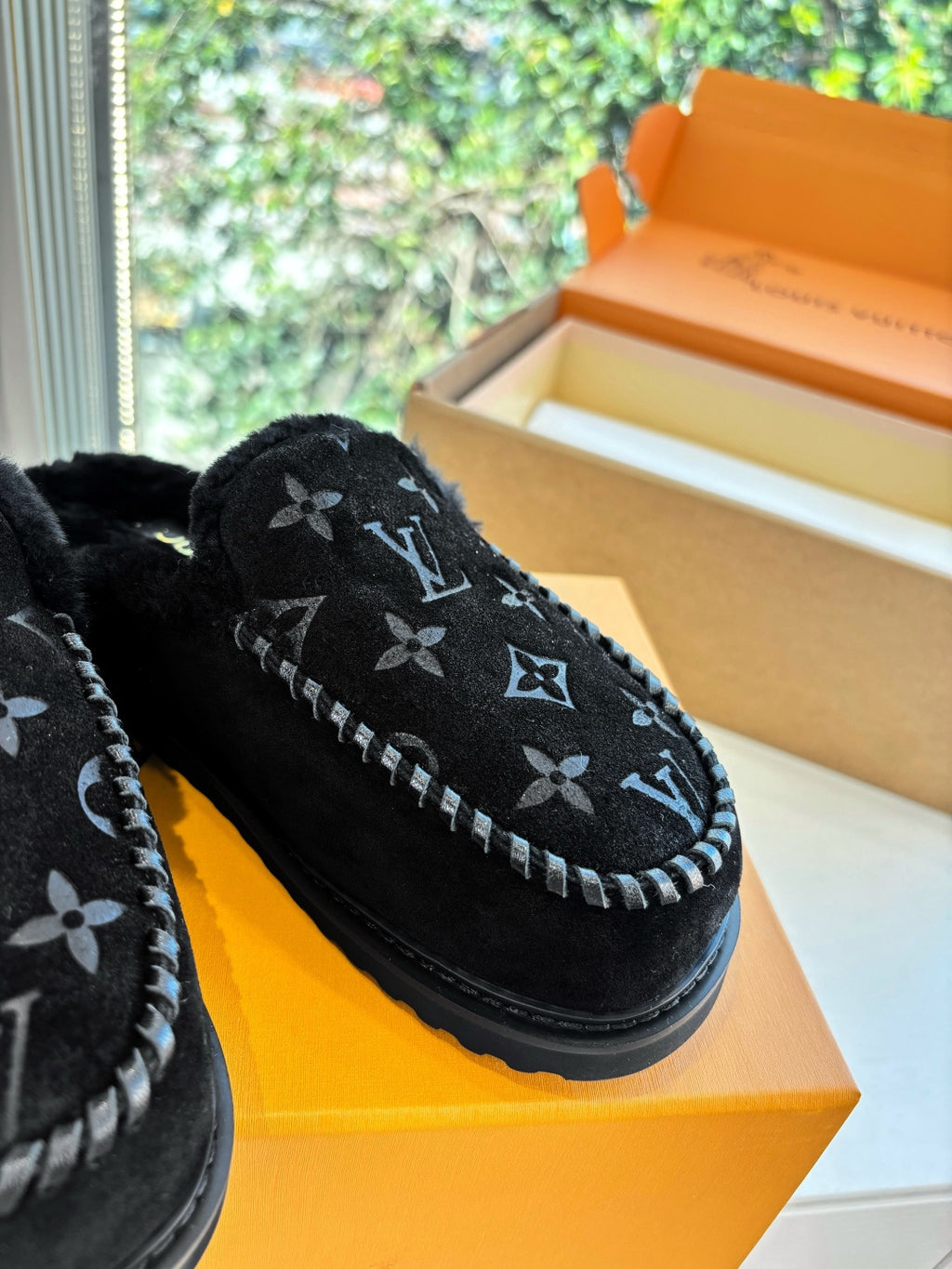 Close-up of black Louis Vuitton monogram slippers with plush upper and stitched trim
