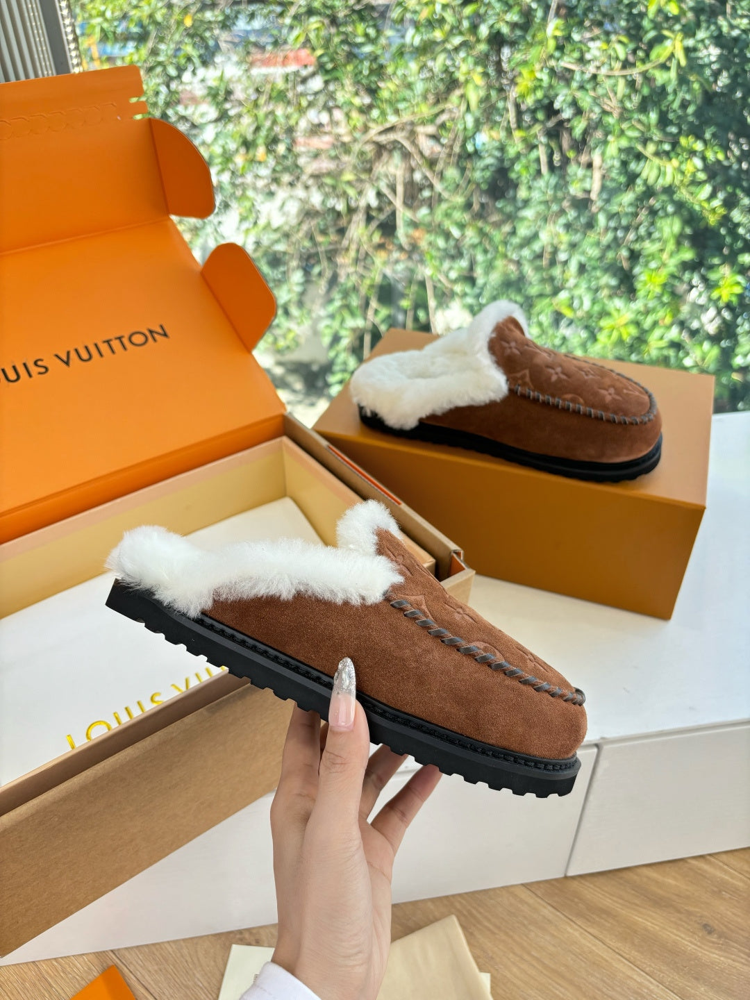 Brown monogram suede shearling slippers with white trim, held in hand