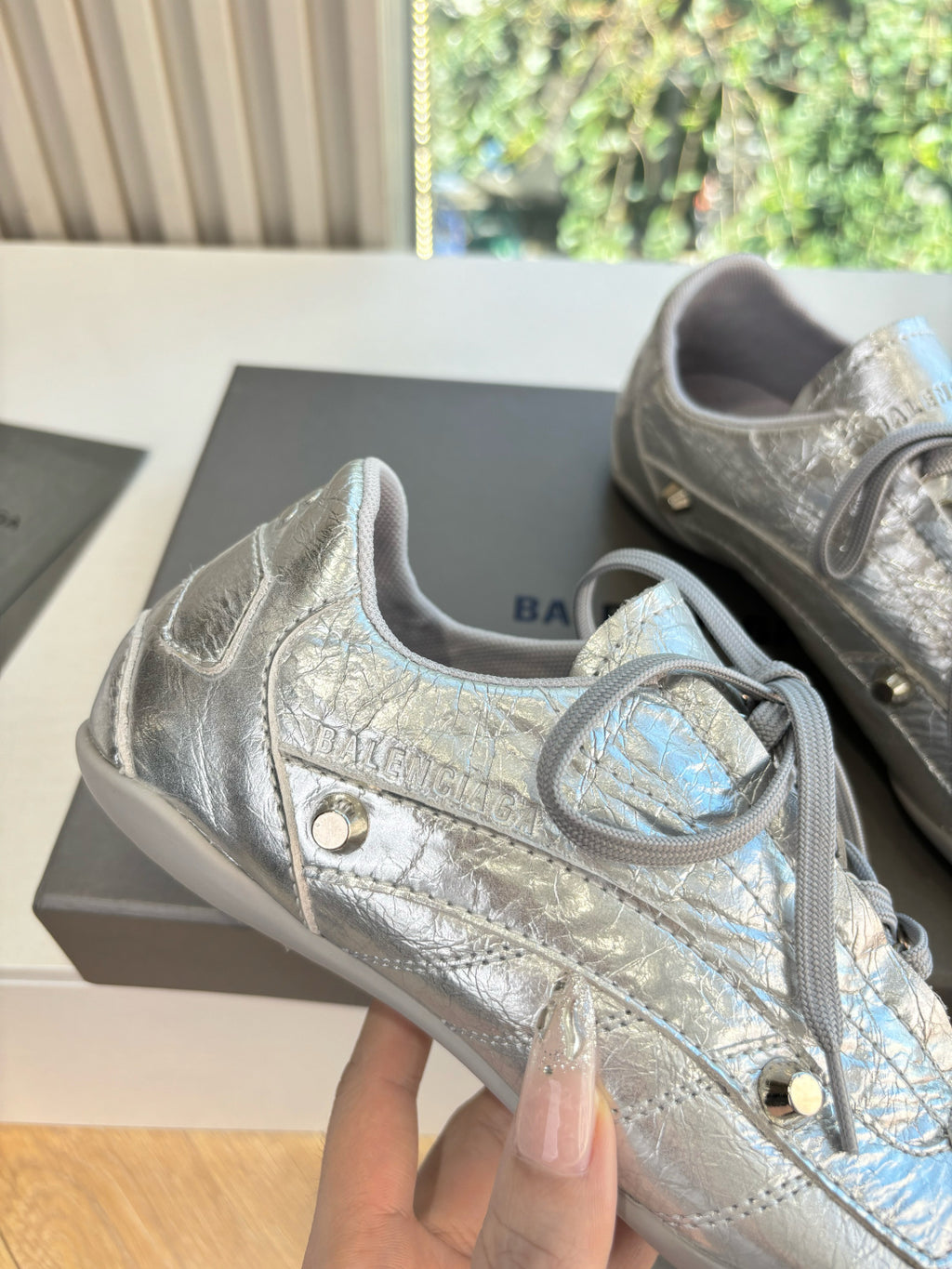 Silver metallic lace-up sneaker close-up with stitched texture and gold eyelet.