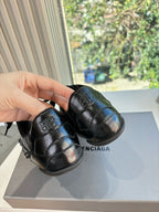 Black leather lace-up sneakers with blue sheen, pair held in hand