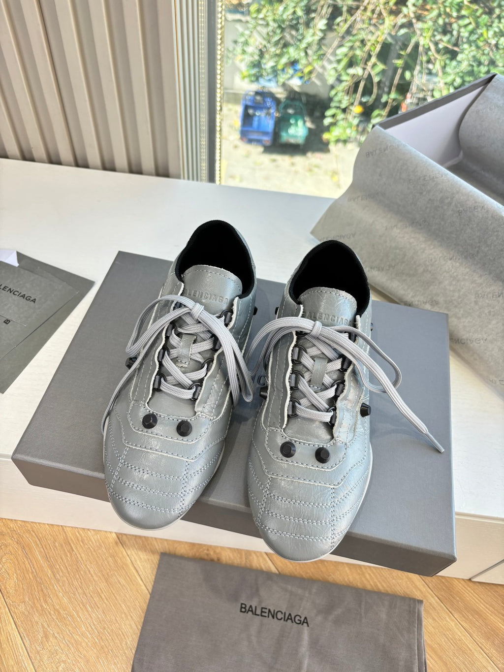 Pair of light gray lace-up sneakers on box, black collars and stitched detailing