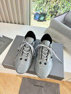 Pair of light gray lace-up sneakers on box, black collars and stitched detailing