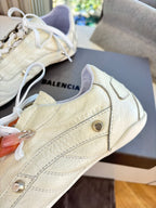 Close-up of cream sneaker with textured leather, metal eyelets, and side stripe seam