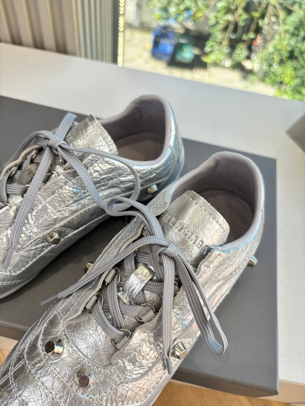 Silver metallic lace-up sneaker close-up with laces, textured pattern, and gold rivets.