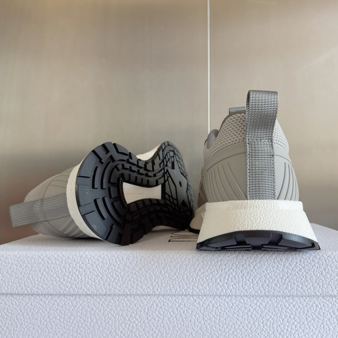 Dior unisex sneakers showing heel and outsole, light gray upper with treaded dark sole