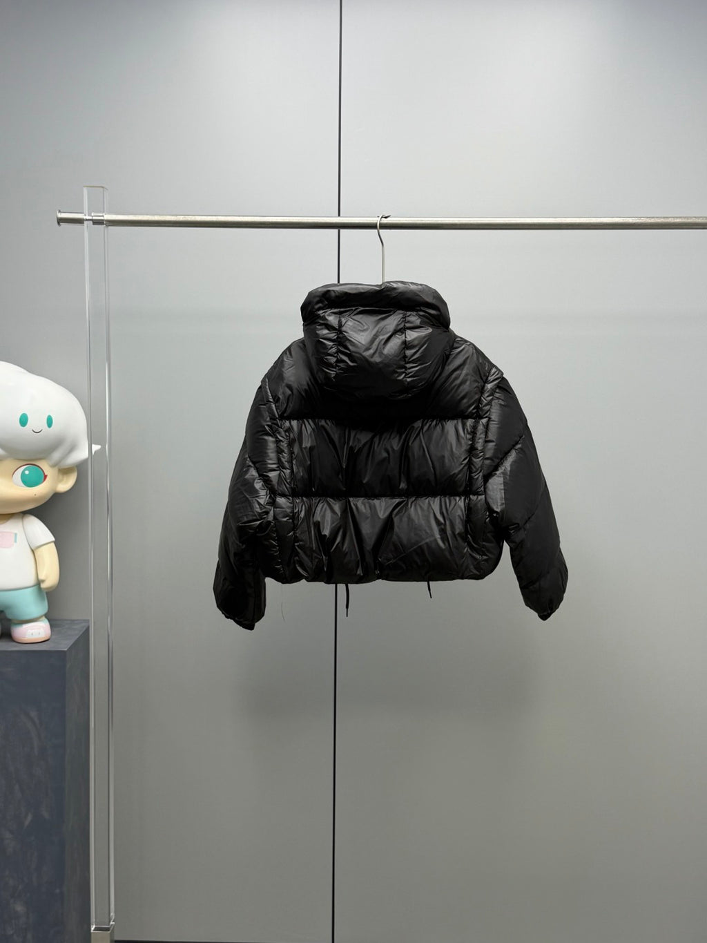 Prada black long puffer jacket with hood and button placket, hanging on rack