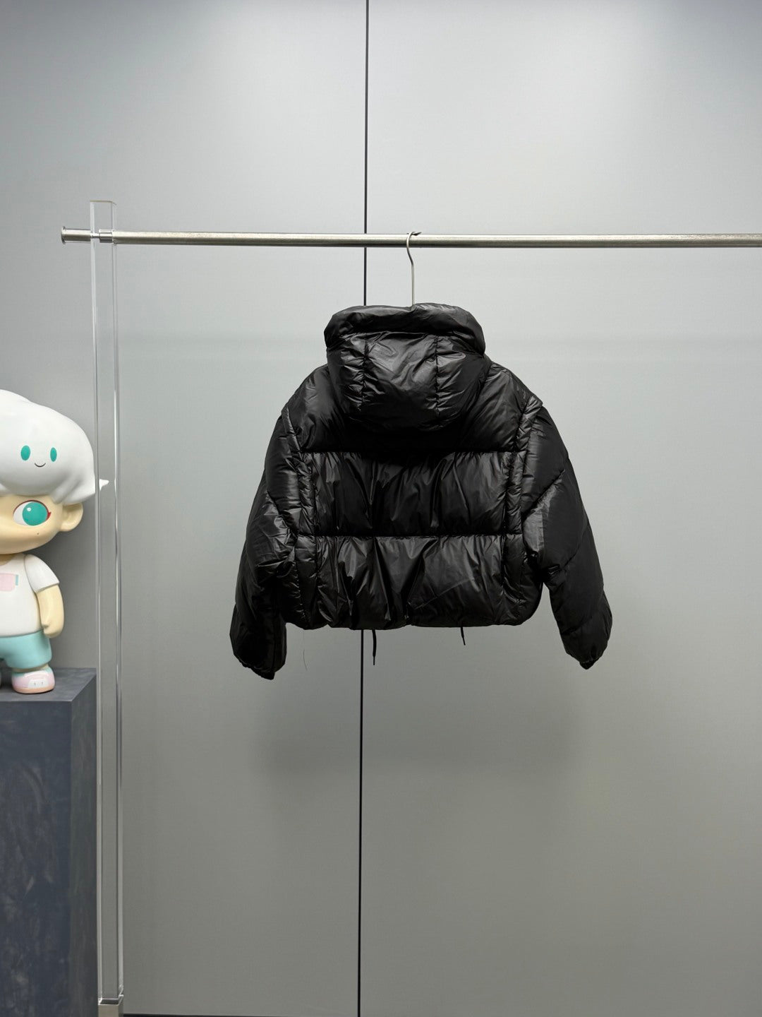 Prada black long puffer jacket with hood and button placket, hanging on rack