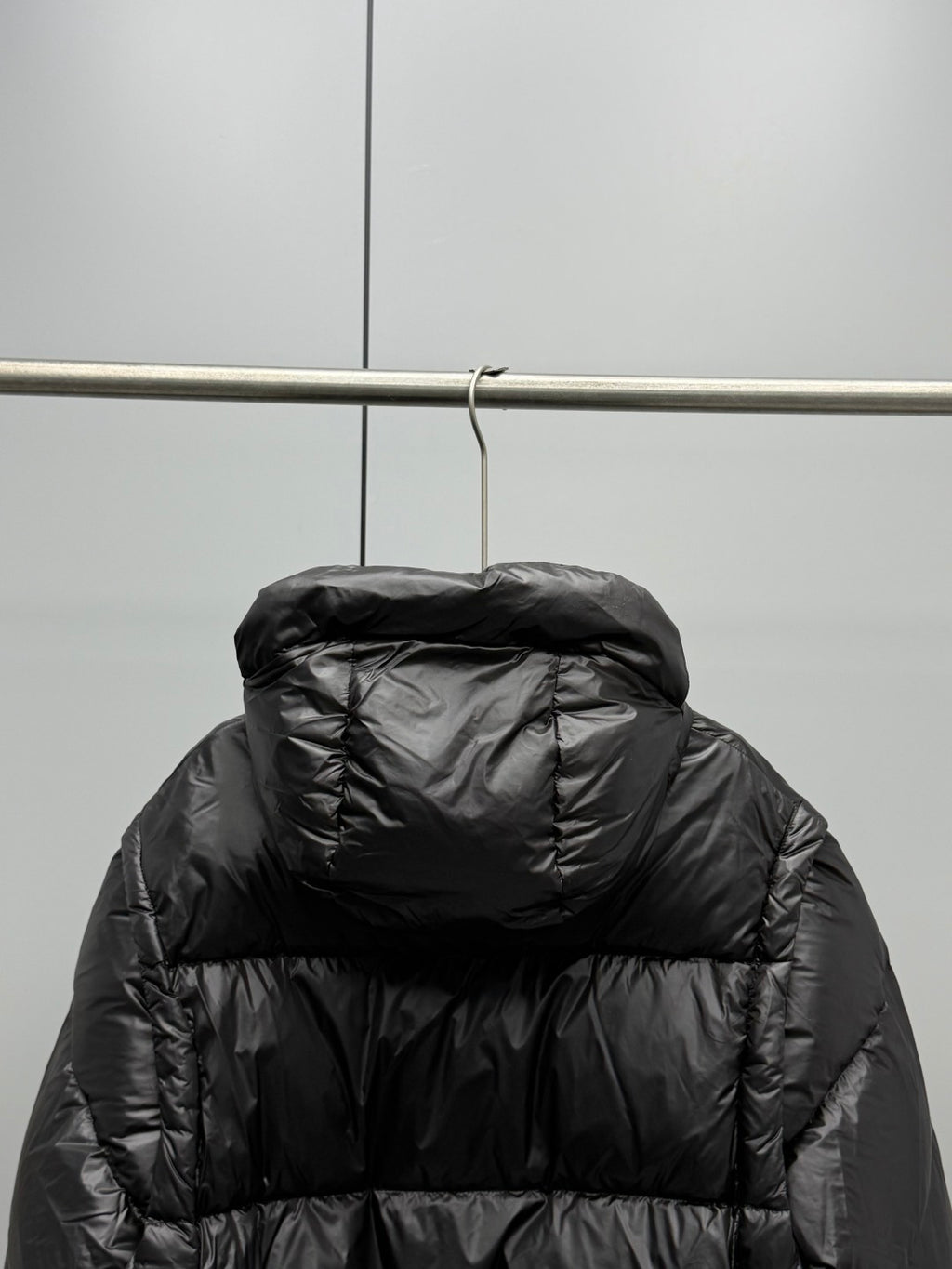 Prada black long puffer jacket back view with hood, hanging on a rack
