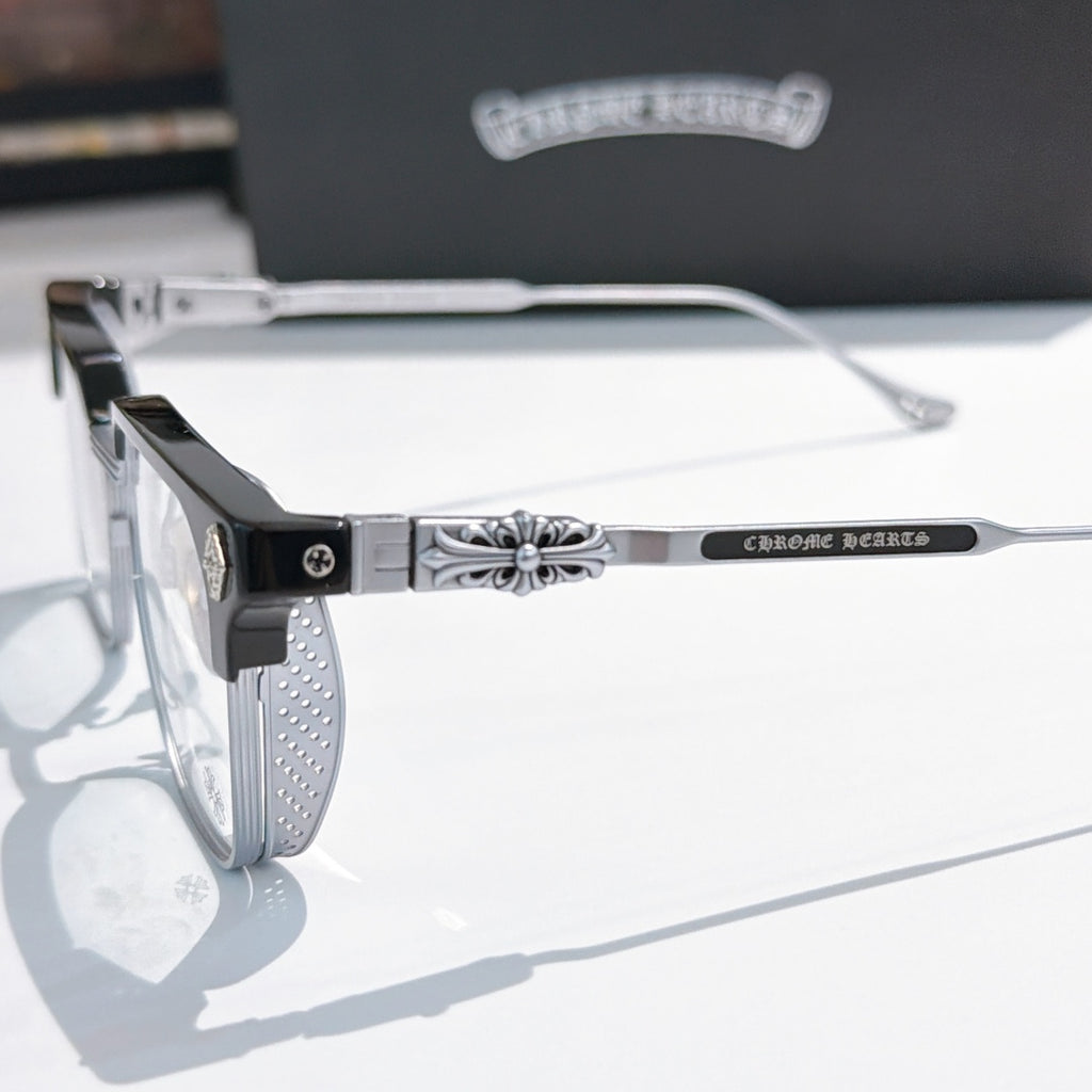 Close-up of black and silver eyeglass frame with patterned temple and clear lens.