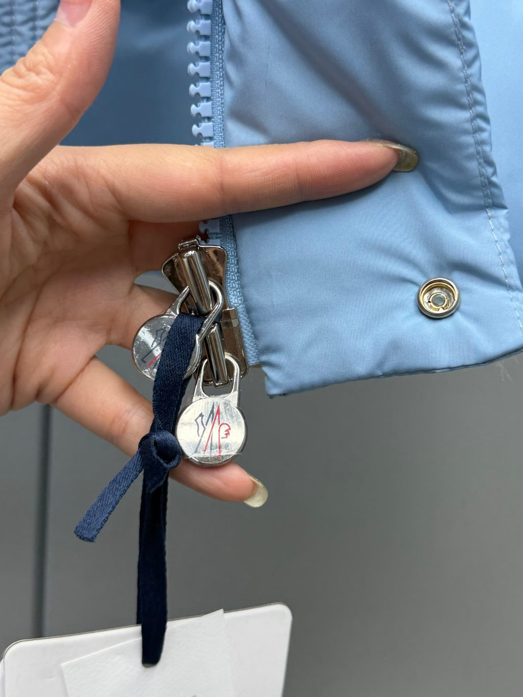 Light blue puffer jacket with gold button placket and hanging keychain tag
