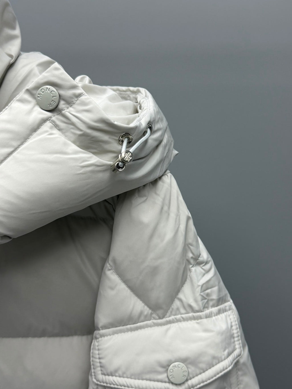 White hooded puffer jacket sleeve with snap buttons and quilted pocket flap