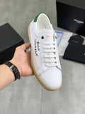 White low-top leather sneakers with green heel trim and beige gum sole.