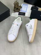 White low-top sneakers with green heel trim, lace-up front, and SAINT LAURENT logo.