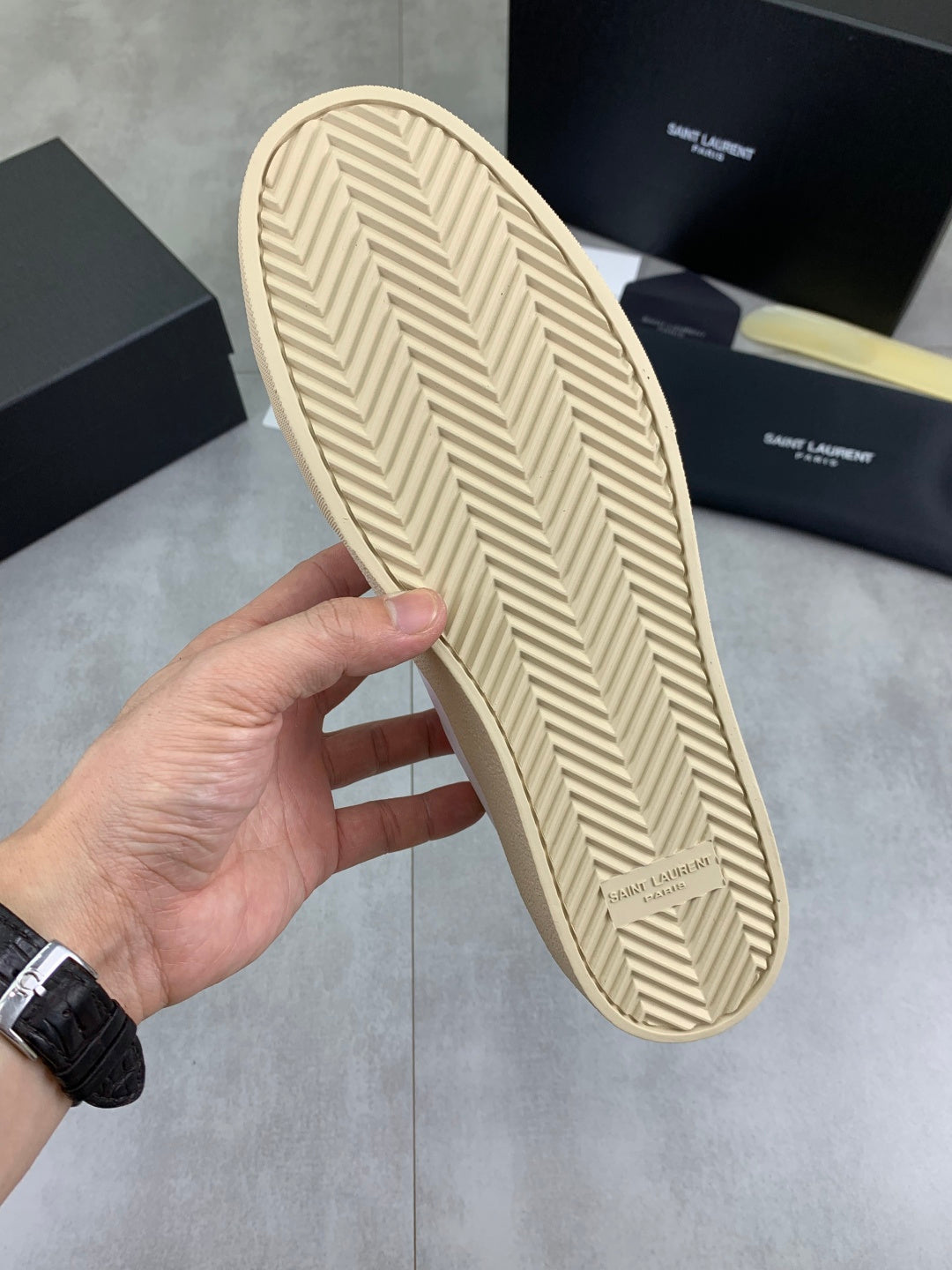 White sneaker outsole with beige herringbone tread and SAINT LAURENT mark.