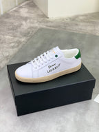 White low-top sneakers with green heel trim, lace-up front, and beige sole.