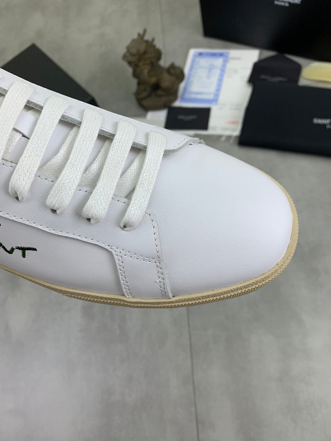 White sneaker toe and lace panel with green SAINT LAURENT logo detail.