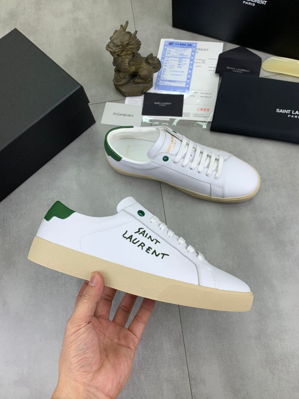 White low-top sneakers with green heel tab and SAINT LAURENT side text.