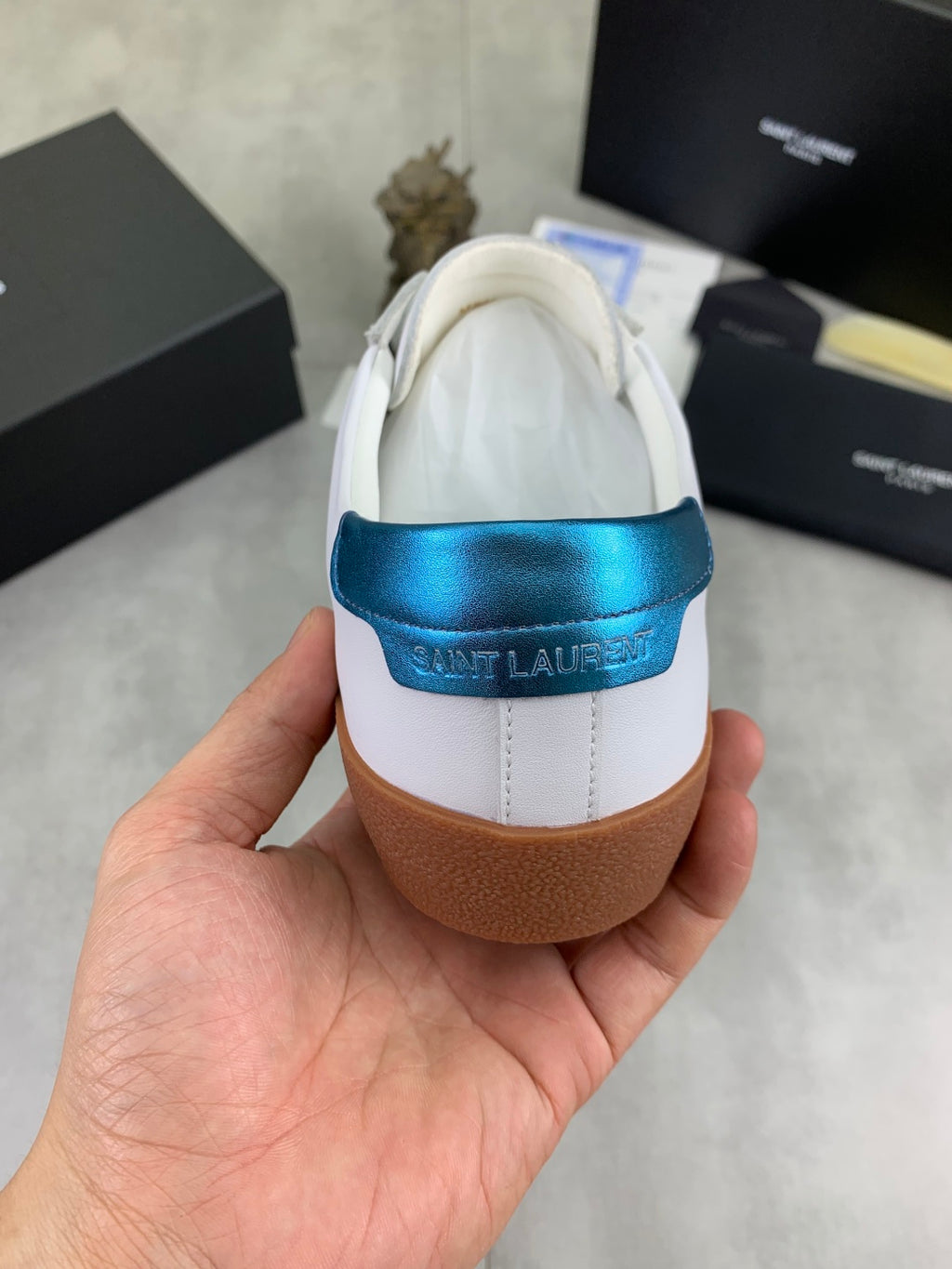 White leather sneaker heel with blue logo strap and brown rubber sole