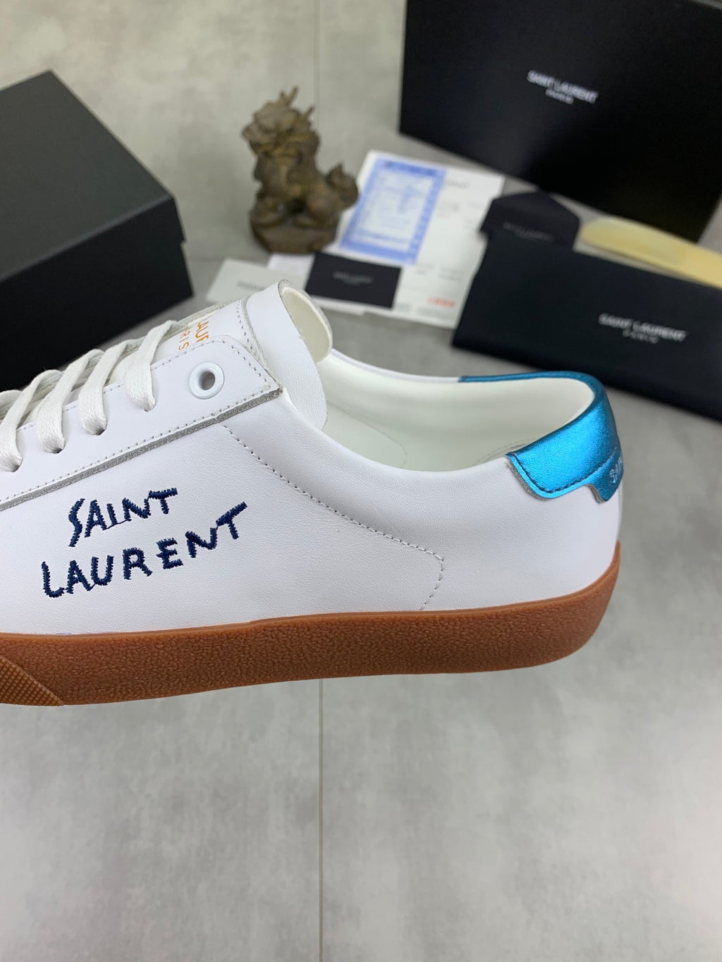 White leather sneaker side with SAINT LAURENT text and blue collar trim