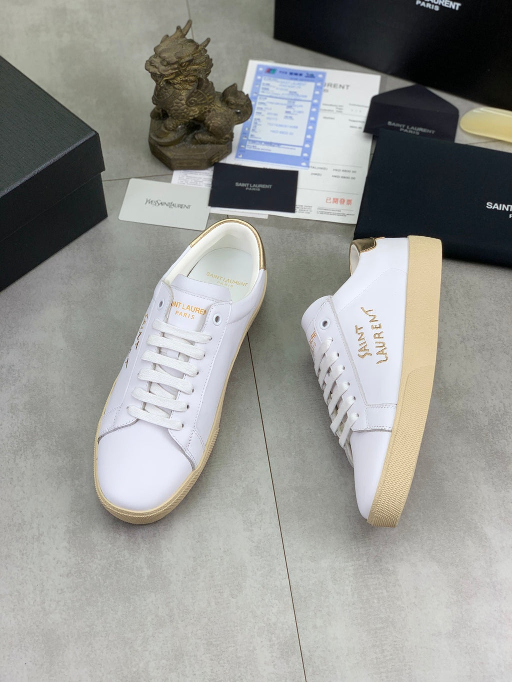 YSL unisex sneakers with white leather uppers, gold writing detail, and tan gum sole.