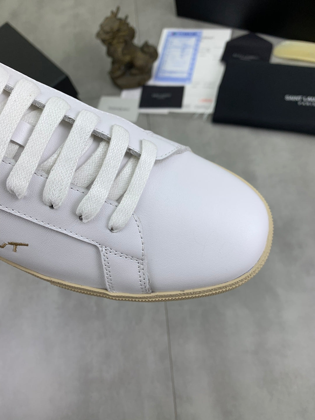 YSL unisex sneakers detail, white lace-up upper with visible stitching and tan edge trim.