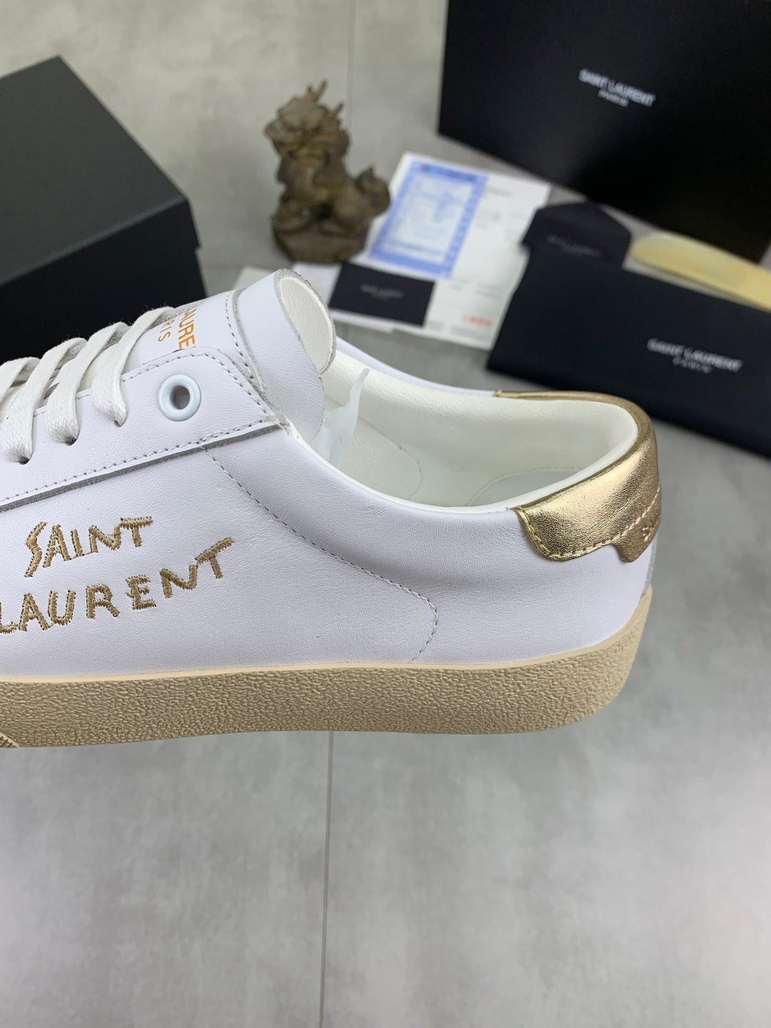 YSL unisex sneakers side view, white upper with gold heel panel and lace eyelets.