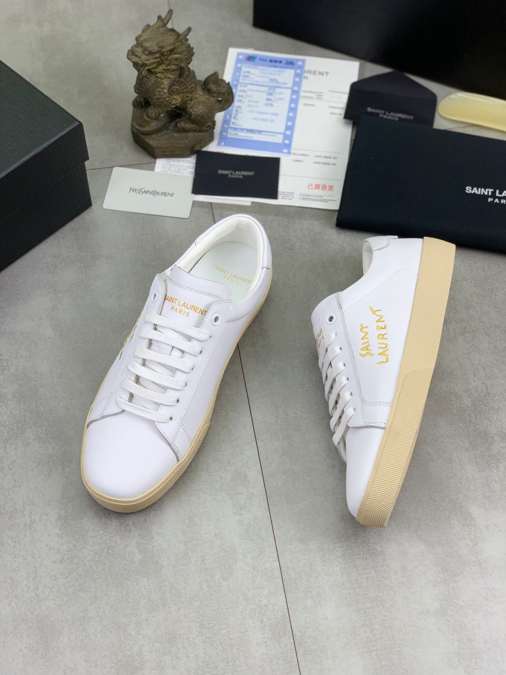 White low-top sneakers with gold Saint Laurent lettering and beige cupsole