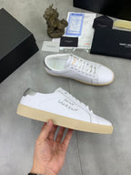 Luxury shoes side view, white upper with white laces and beige rubber sole.