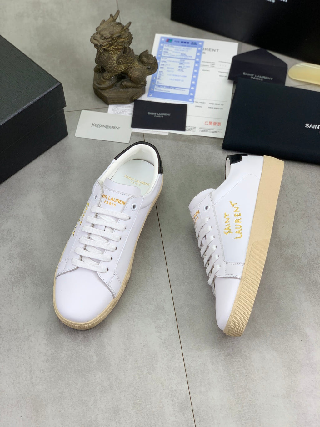 White low-top sneaker with gold side lettering and off-white rubber sole