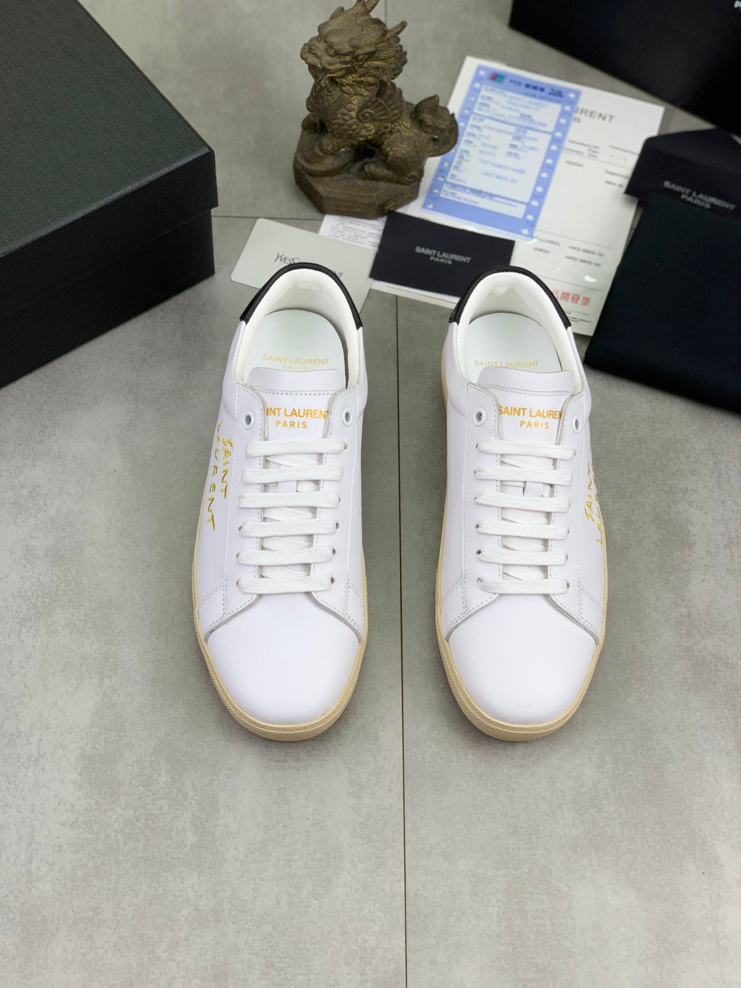 Pair of white low-top sneakers with gold side text and gum rubber soles