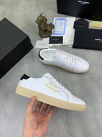 White low-top sneaker with gold side lettering, black heel accent, gum sole