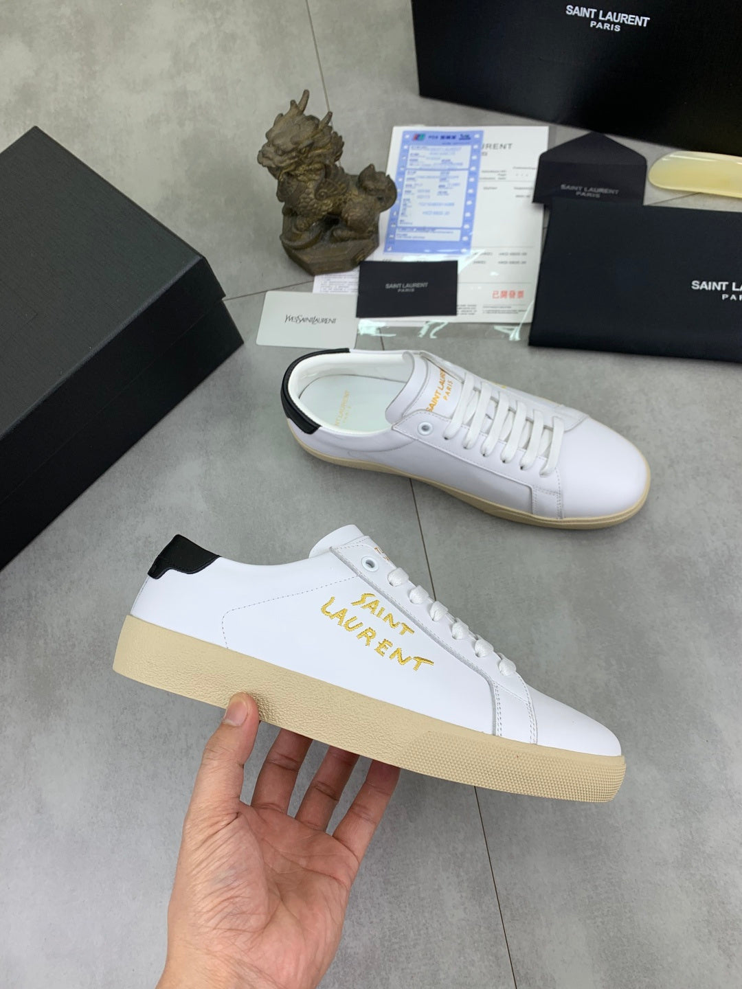 White low-top sneaker with gold side lettering, black heel accent, gum sole