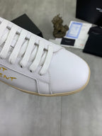 Close-up of white low-top sneaker with gold side lettering and white laces