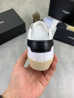 Back view of white low-top sneaker with black strap and beige rubber sole