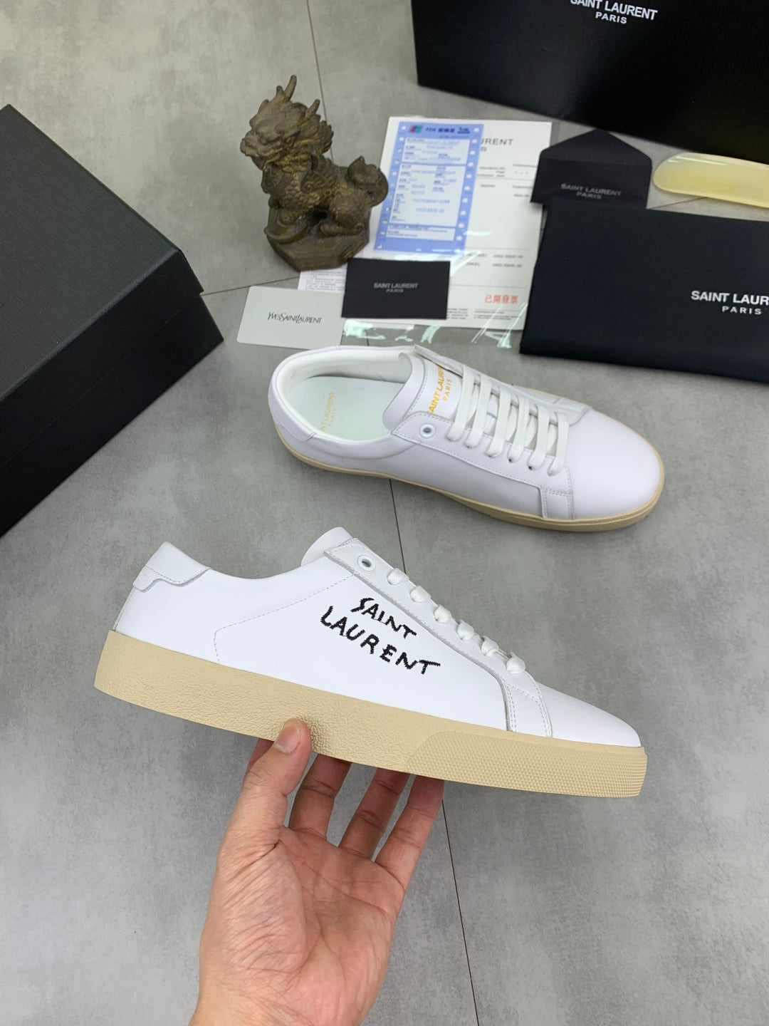 White YSL unisex sneakers held in hand, side logo and gum rubber sole