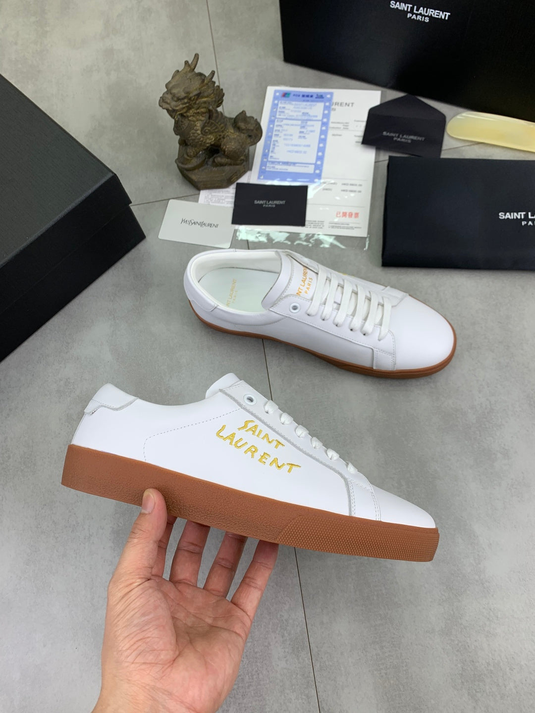 White low-top sneakers with gold logo and tan rubber soles