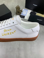 Close-up of white low-top sneaker side with gold “SAINT LAURENT” text and tan sole
