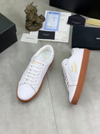 White low-top sneakers with gold logo stitching and tan rubber soles