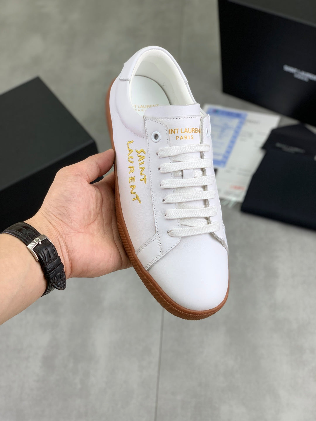 Low-top sneakers in white leather with gold logo, white laces, and tan rubber sole