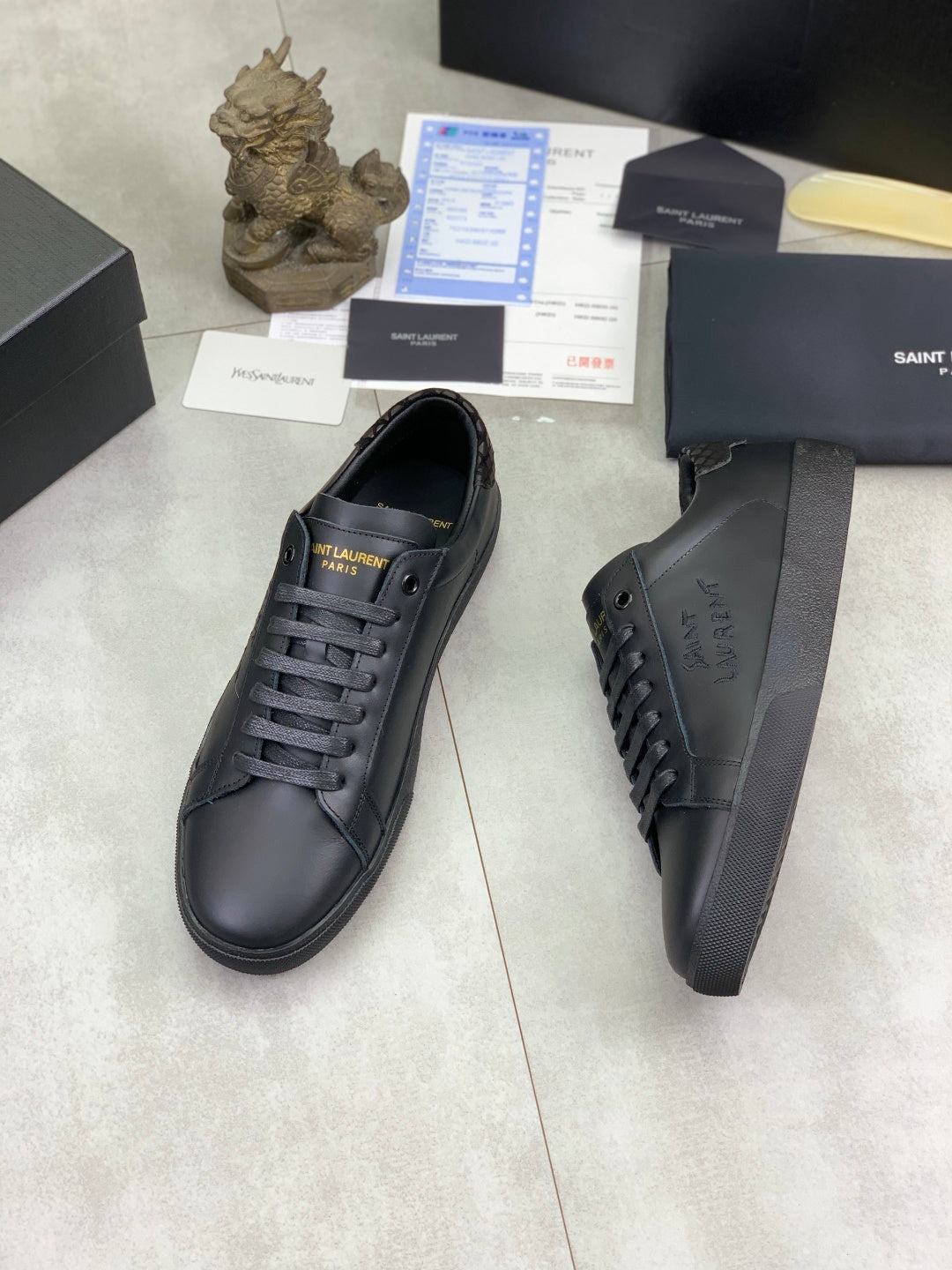 Dark leather lace-up sneakers showing side logos and textured heel area.